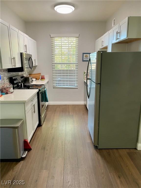 kitchen featuring light wood-style flooring, stainless steel appliances, white cabinetry, light countertops, and tasteful backsplash