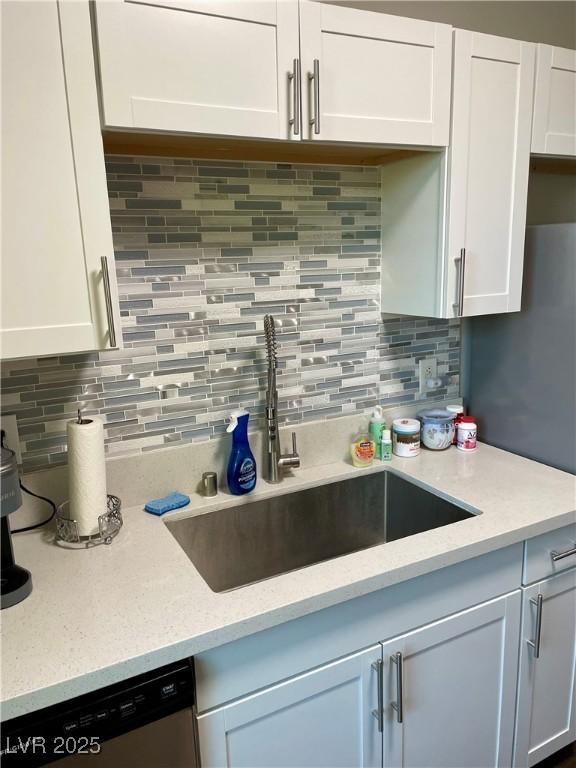 kitchen featuring decorative backsplash, dishwasher, light stone countertops, white cabinetry, and a sink