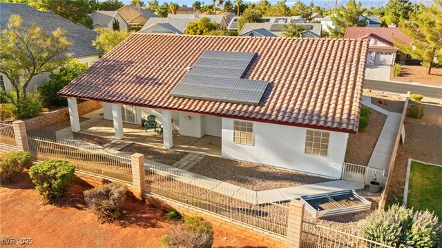 back of property featuring a tile roof, stucco siding, roof mounted solar panels, fence, and a residential view