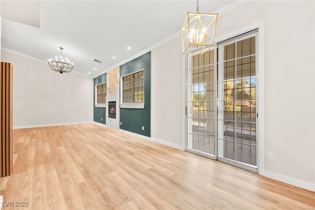 interior space with light wood-style floors, a large fireplace, a notable chandelier, and ornamental molding