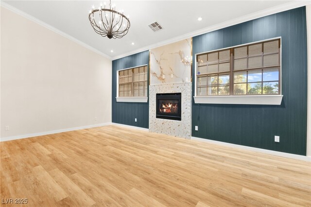 unfurnished living room featuring visible vents, a glass covered fireplace, ornamental molding, wood finished floors, and a chandelier