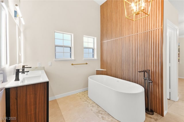 full bathroom with double vanity, a freestanding bath, a sink, tile patterned flooring, and baseboards