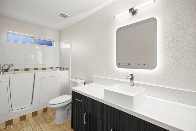 bathroom with toilet, a washtub, wood finish floors, vanity, and visible vents