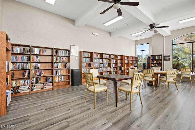 interior space with wall of books, a ceiling fan, beam ceiling, and wood finished floors