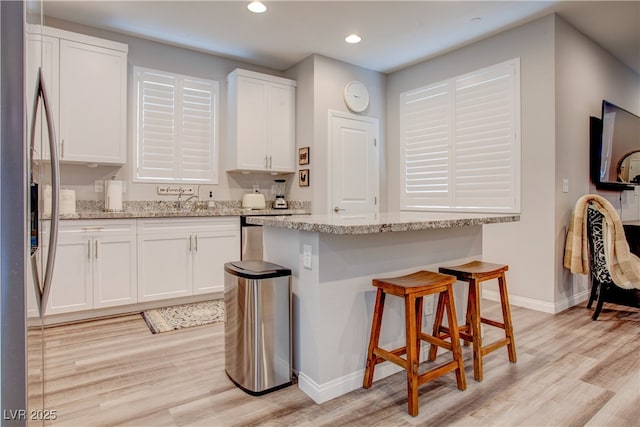 kitchen with light wood-type flooring, light stone countertops, and white cabinets