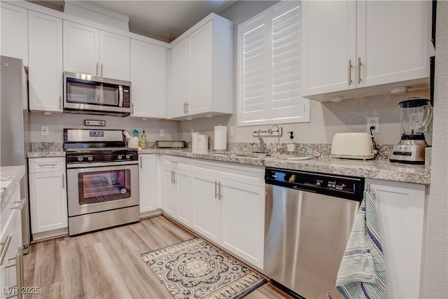 kitchen featuring light wood finished floors, white cabinetry, appliances with stainless steel finishes, and light stone counters