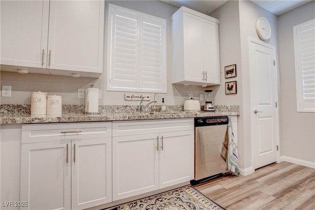 kitchen featuring light stone counters, light wood finished floors, stainless steel dishwasher, white cabinets, and a sink