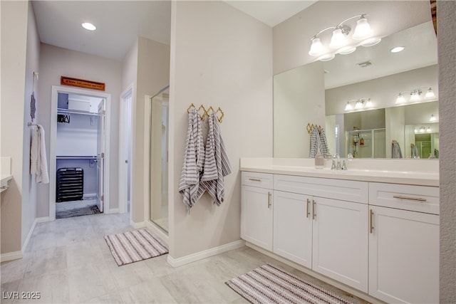 bathroom with a stall shower, baseboards, a walk in closet, and vanity