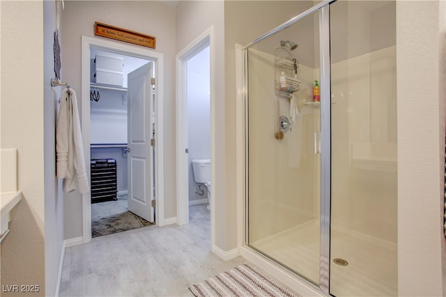 full bath featuring a walk in closet, toilet, a shower stall, wood finished floors, and baseboards