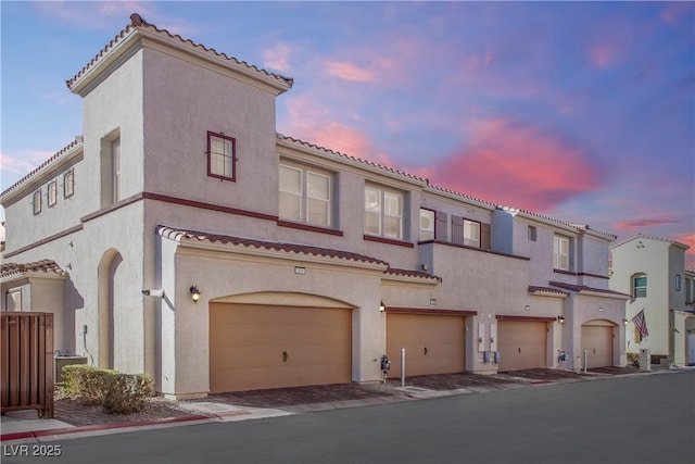 mediterranean / spanish-style home with a garage, a tiled roof, and stucco siding