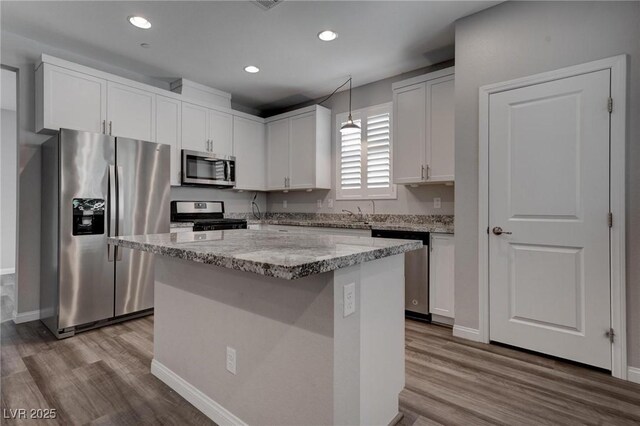 kitchen featuring a center island, wood finished floors, white cabinets, light stone countertops, and appliances with stainless steel finishes