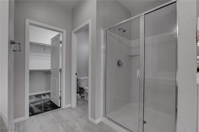 full bathroom featuring a stall shower, baseboards, toilet, and a walk in closet
