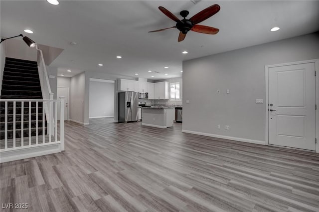 unfurnished living room with a ceiling fan, recessed lighting, stairway, baseboards, and light wood-style floors