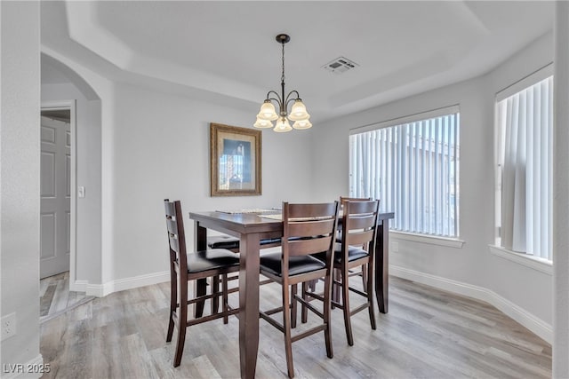 dining space with baseboards, visible vents, arched walkways, light wood-type flooring, and a notable chandelier