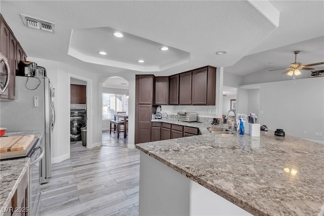 kitchen featuring light stone countertops, a tray ceiling, visible vents, and a sink