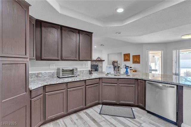 kitchen featuring light stone counters, a toaster, a sink, dishwasher, and a peninsula