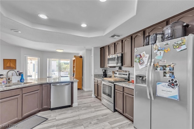 kitchen with a tray ceiling, visible vents, appliances with stainless steel finishes, a sink, and light stone countertops