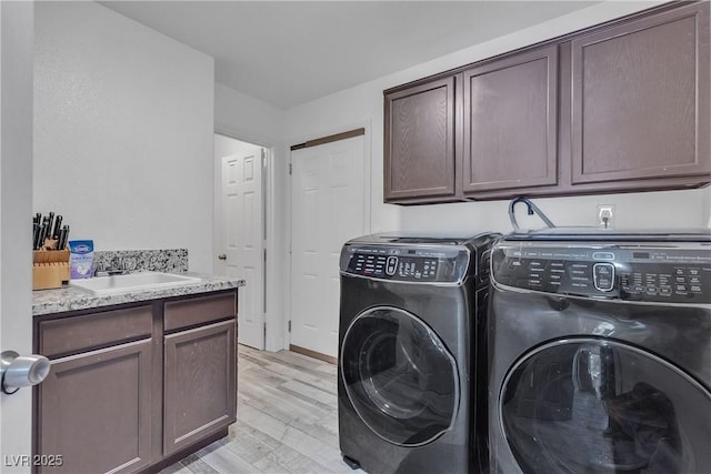 laundry room featuring light wood-type flooring, cabinet space, a sink, and washing machine and clothes dryer