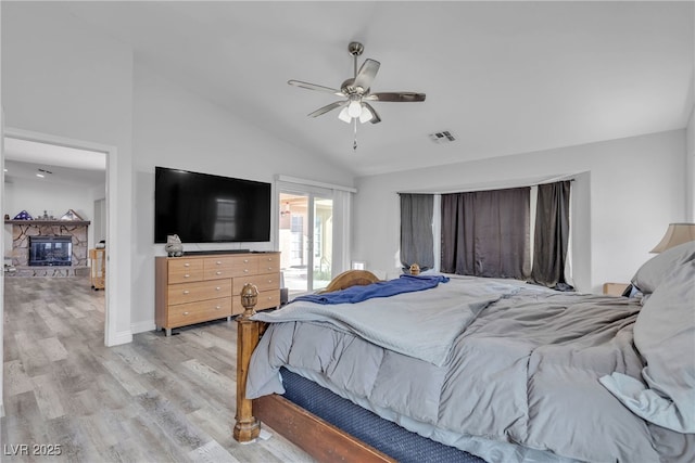 bedroom with lofted ceiling, visible vents, ceiling fan, a stone fireplace, and light wood-type flooring