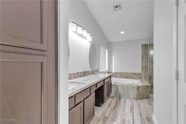 bathroom featuring a garden tub, double vanity, visible vents, a sink, and wood finished floors