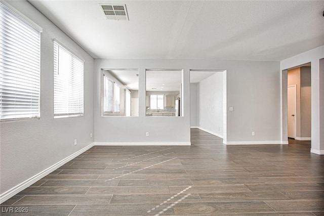 empty room with dark wood-type flooring, plenty of natural light, visible vents, and baseboards