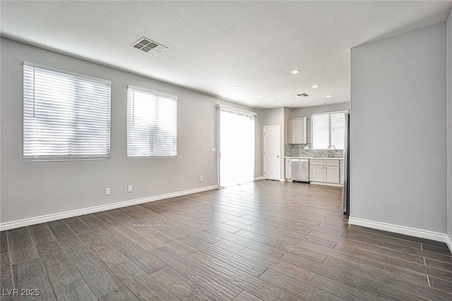 unfurnished living room featuring a sink, baseboards, visible vents, and dark wood-type flooring