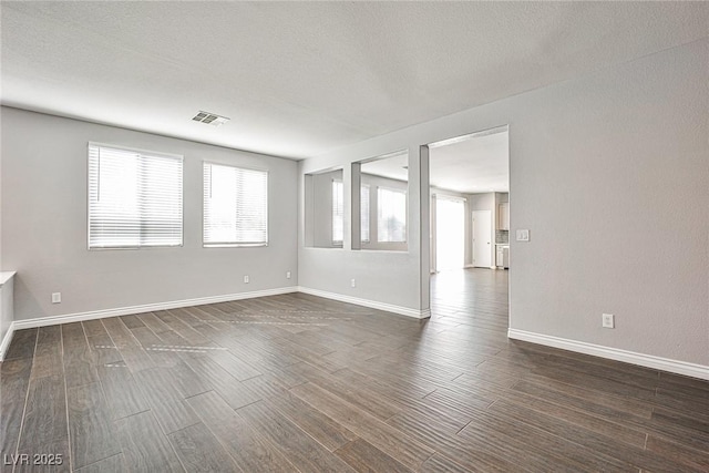 empty room featuring dark wood-type flooring, visible vents, a textured ceiling, and baseboards