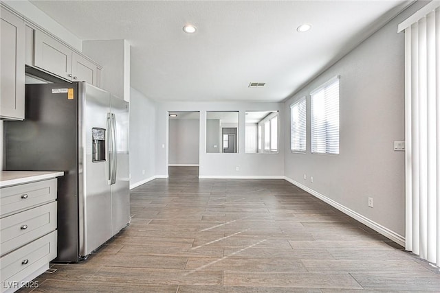 interior space with wood finished floors, visible vents, baseboards, light countertops, and stainless steel fridge with ice dispenser