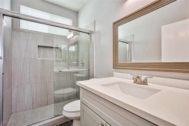 bathroom featuring a textured wall, a stall shower, vanity, and toilet