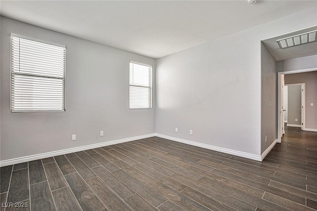 empty room with dark wood-style flooring, visible vents, and baseboards