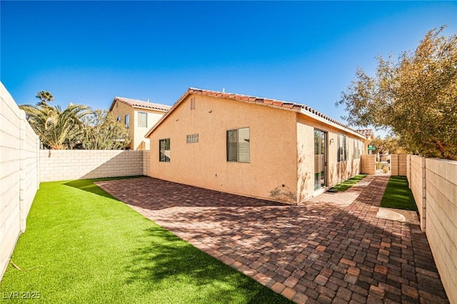 view of side of property featuring a yard, stucco siding, a patio area, a fenced backyard, and a tiled roof