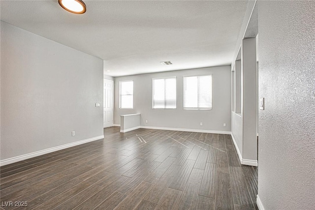 unfurnished room featuring a textured ceiling, dark wood-type flooring, visible vents, and baseboards