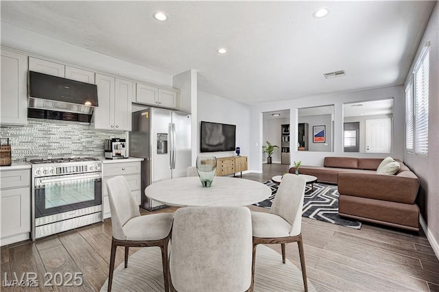 kitchen with tasteful backsplash, appliances with stainless steel finishes, light wood-style flooring, and range hood