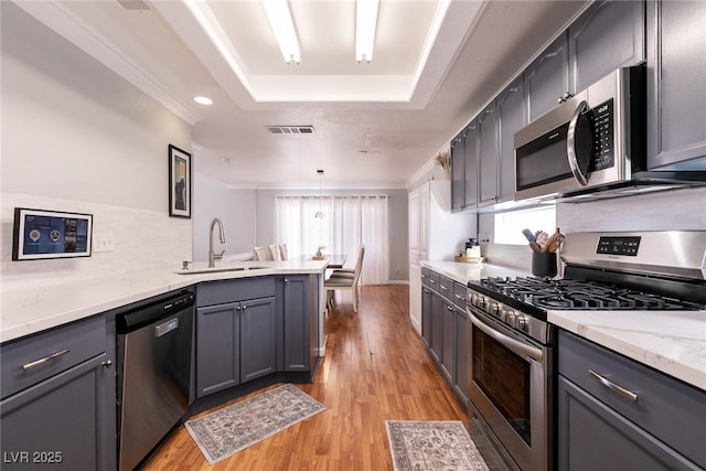 kitchen with a tray ceiling, visible vents, hanging light fixtures, gray cabinetry, and appliances with stainless steel finishes