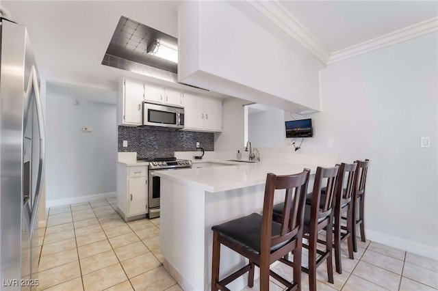 kitchen featuring white cabinets, a peninsula, stainless steel appliances, light countertops, and backsplash