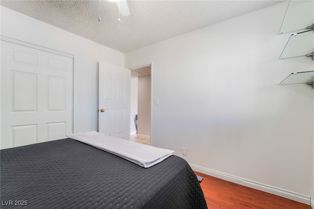 unfurnished bedroom with ceiling fan, a textured ceiling, baseboards, and wood finished floors