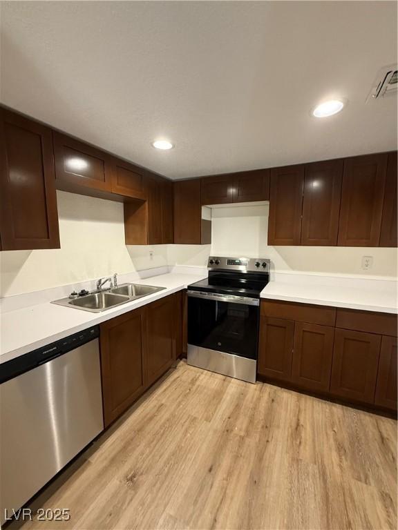 kitchen with stainless steel appliances, light wood-type flooring, light countertops, and a sink