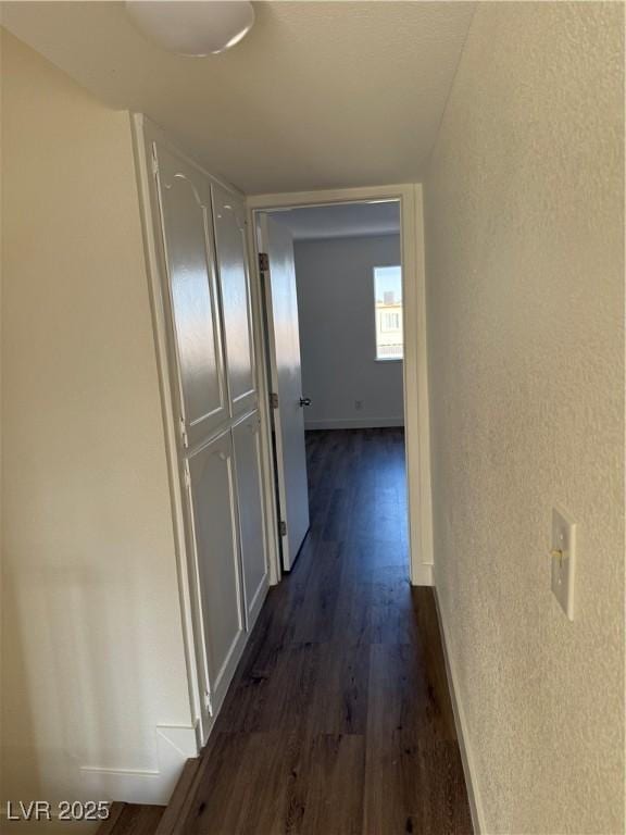 corridor featuring dark wood-style floors, baseboards, and a textured wall