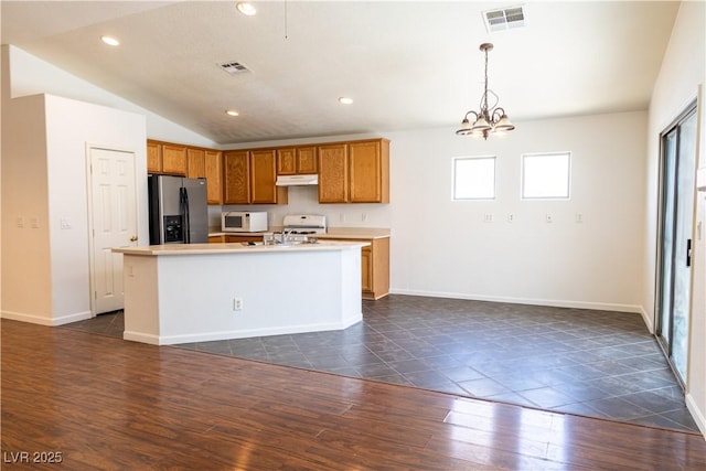 kitchen with light countertops, visible vents, white microwave, an island with sink, and stainless steel fridge