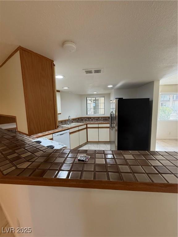 kitchen with white dishwasher, a sink, visible vents, freestanding refrigerator, and tile counters