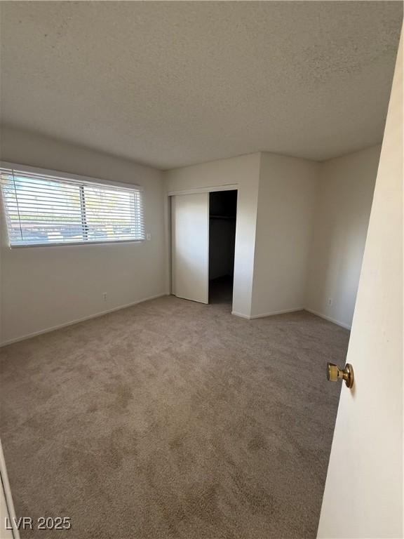 unfurnished bedroom featuring carpet, a closet, baseboards, and a textured ceiling