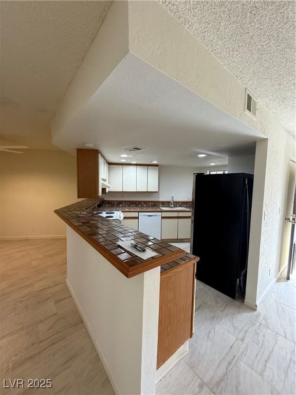 kitchen with a peninsula, white cabinetry, freestanding refrigerator, tile counters, and dishwasher