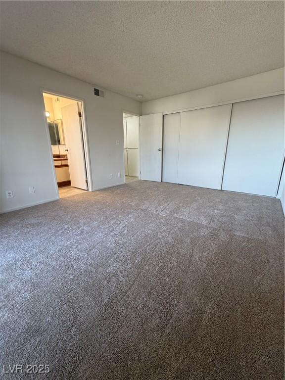 unfurnished bedroom with a closet, visible vents, light carpet, and a textured ceiling