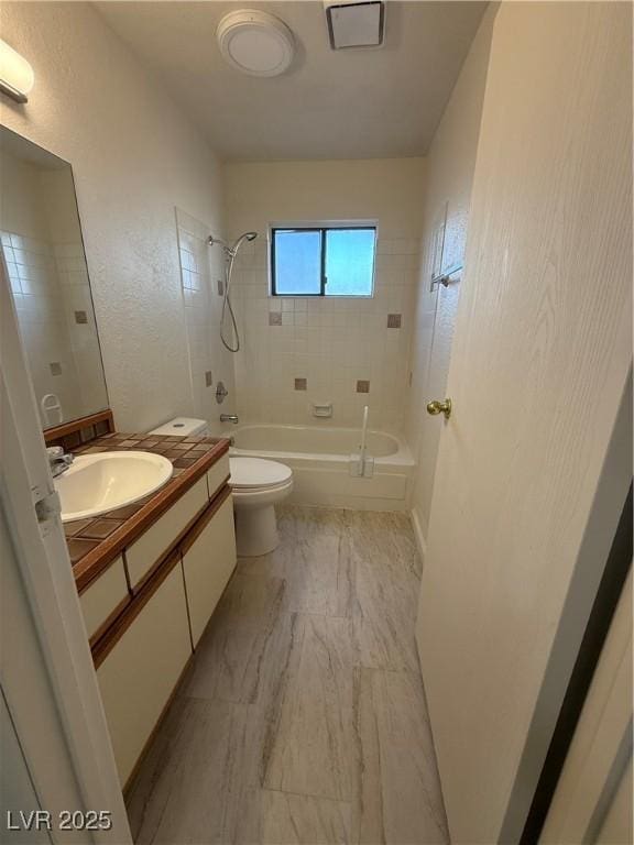 bathroom with tub / shower combination, a textured wall, vanity, and toilet