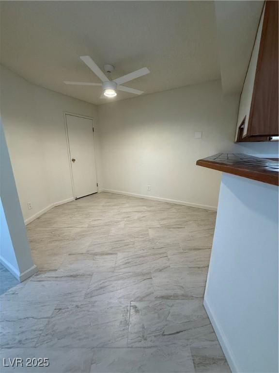 unfurnished room featuring ceiling fan, marble finish floor, and baseboards