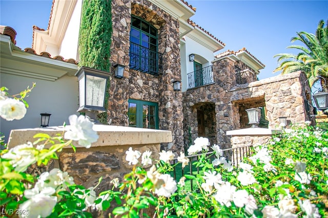 exterior space featuring a tiled roof, stone siding, a balcony, and stucco siding