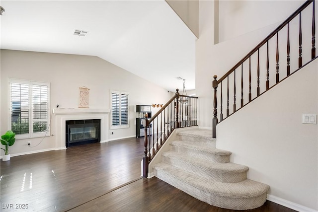 staircase featuring baseboards, visible vents, wood finished floors, a fireplace, and high vaulted ceiling