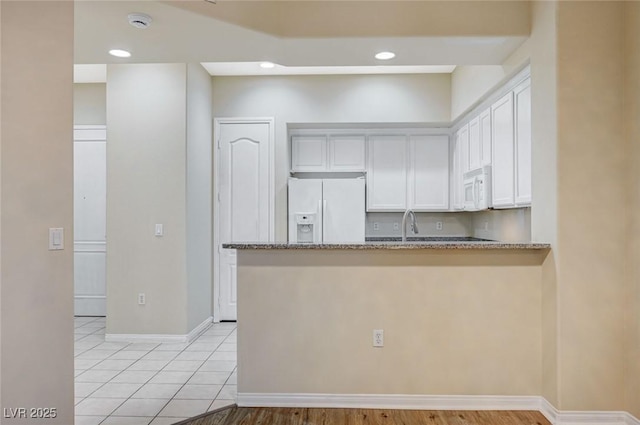 kitchen featuring white appliances, baseboards, white cabinets, a peninsula, and light stone countertops