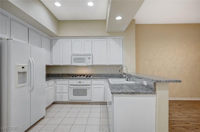 kitchen with white cabinets, a sink, dark stone countertops, white appliances, and a peninsula