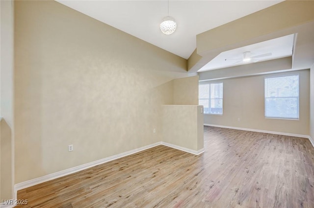 spare room featuring lofted ceiling, light wood finished floors, and baseboards